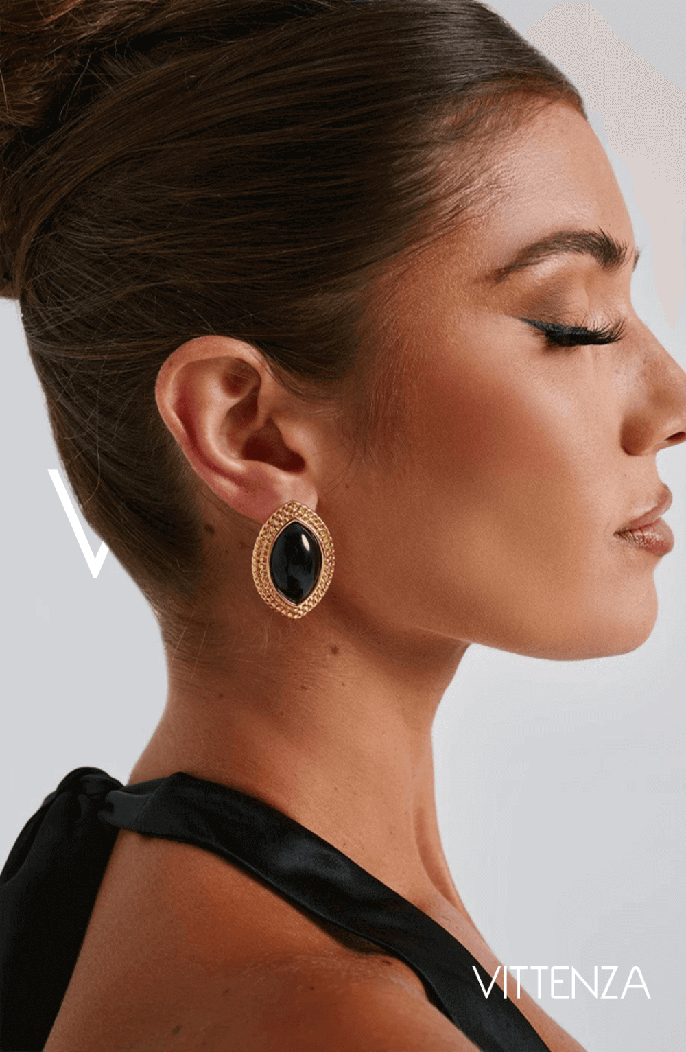 Profile view of a model wearing Azra Earrings in black with a textured gold frame, showcasing the sophisticated ellipse design.