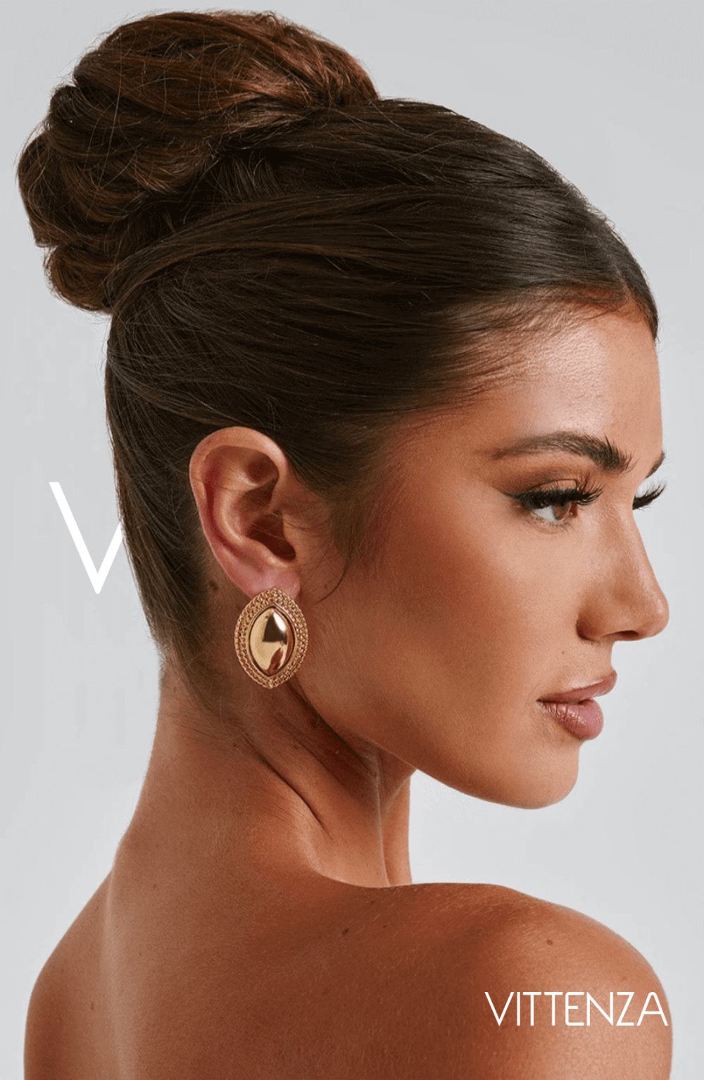 Side view of a model wearing Azra Earrings in gold with a smooth metallic center and textured gold frame, showcasing the timeless ellipse design.