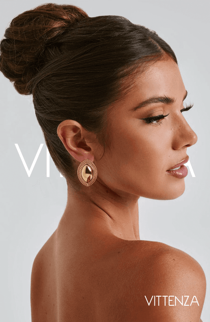 Model wearing Azra Earrings in gold with a smooth metallic center and textured gold frame, showcasing a sophisticated ellipse shape.