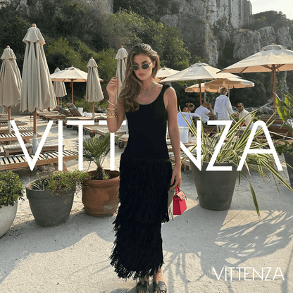 Front view of the black Bahamas dress worn by a model at a stylish beachside location, accessorized with a red handbag and statement sunglasses.