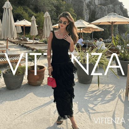 Model wearing the black Bahamas dress outdoors at a chic beachside venue, paired with a red handbag and sunglasses.