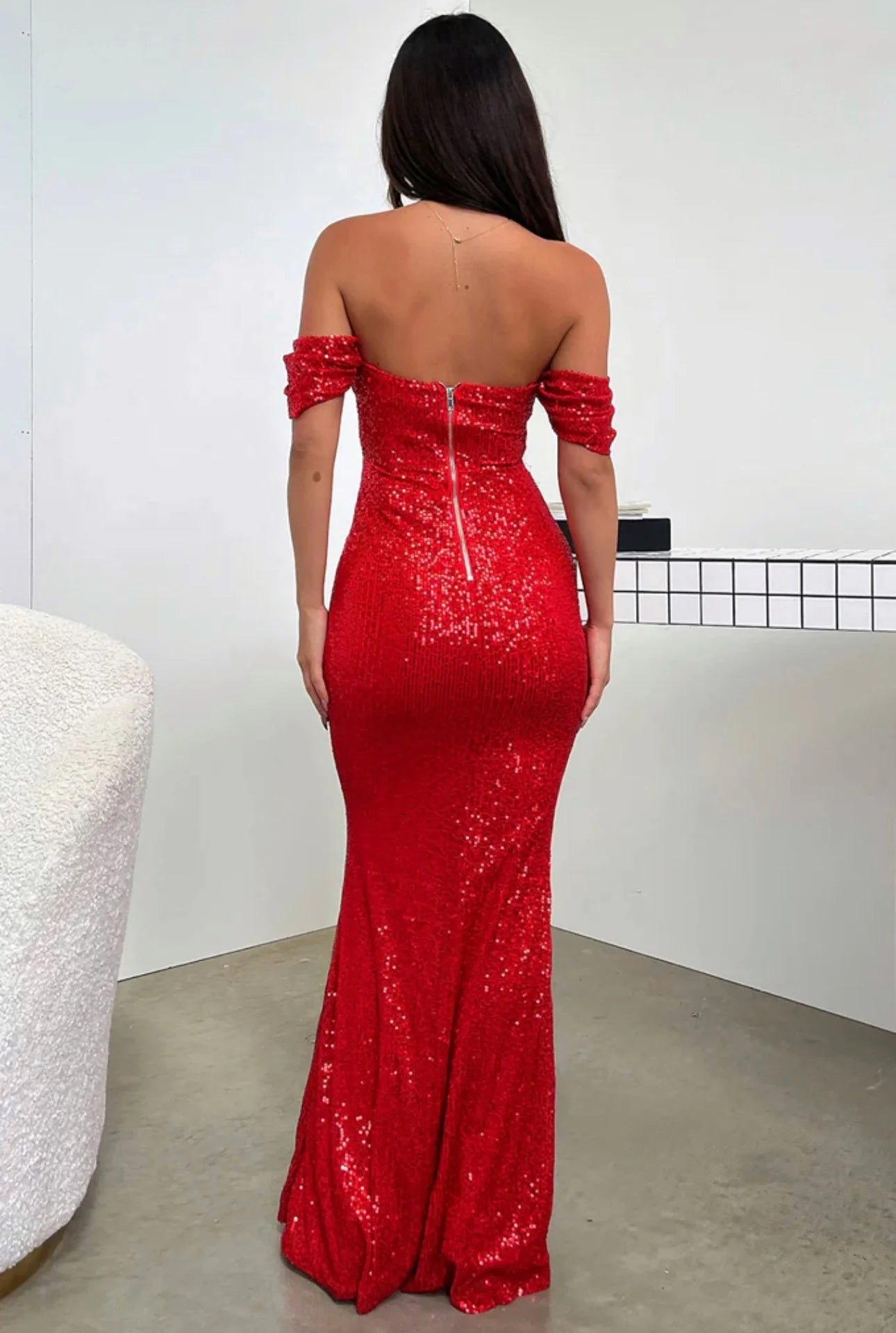 Back view of the red sequined off-shoulder evening gown, highlighting the zip closure, fitted silhouette, and elegant drape.