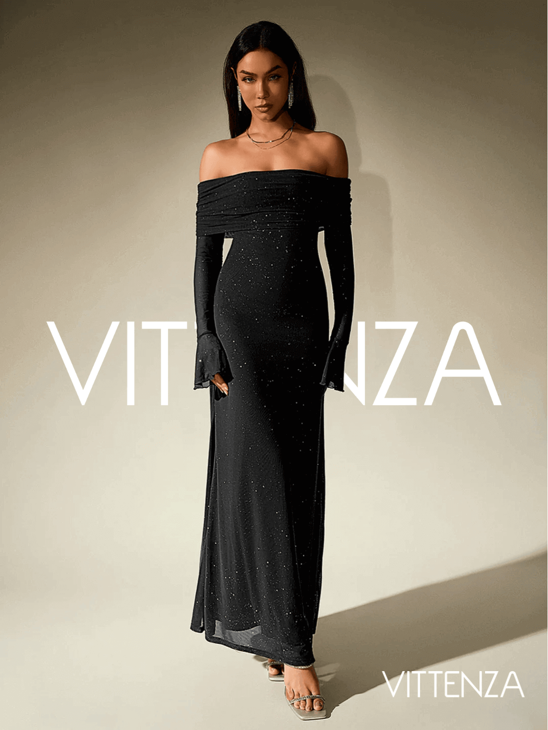 Front view of the Stellar Sparkle Maxi Dress in shimmering black. The dress features an off-shoulder design, glittering details, long sleeves with flared cuffs, and a floor-length silhouette. The model accessorizes with metallic heels and layered necklaces.