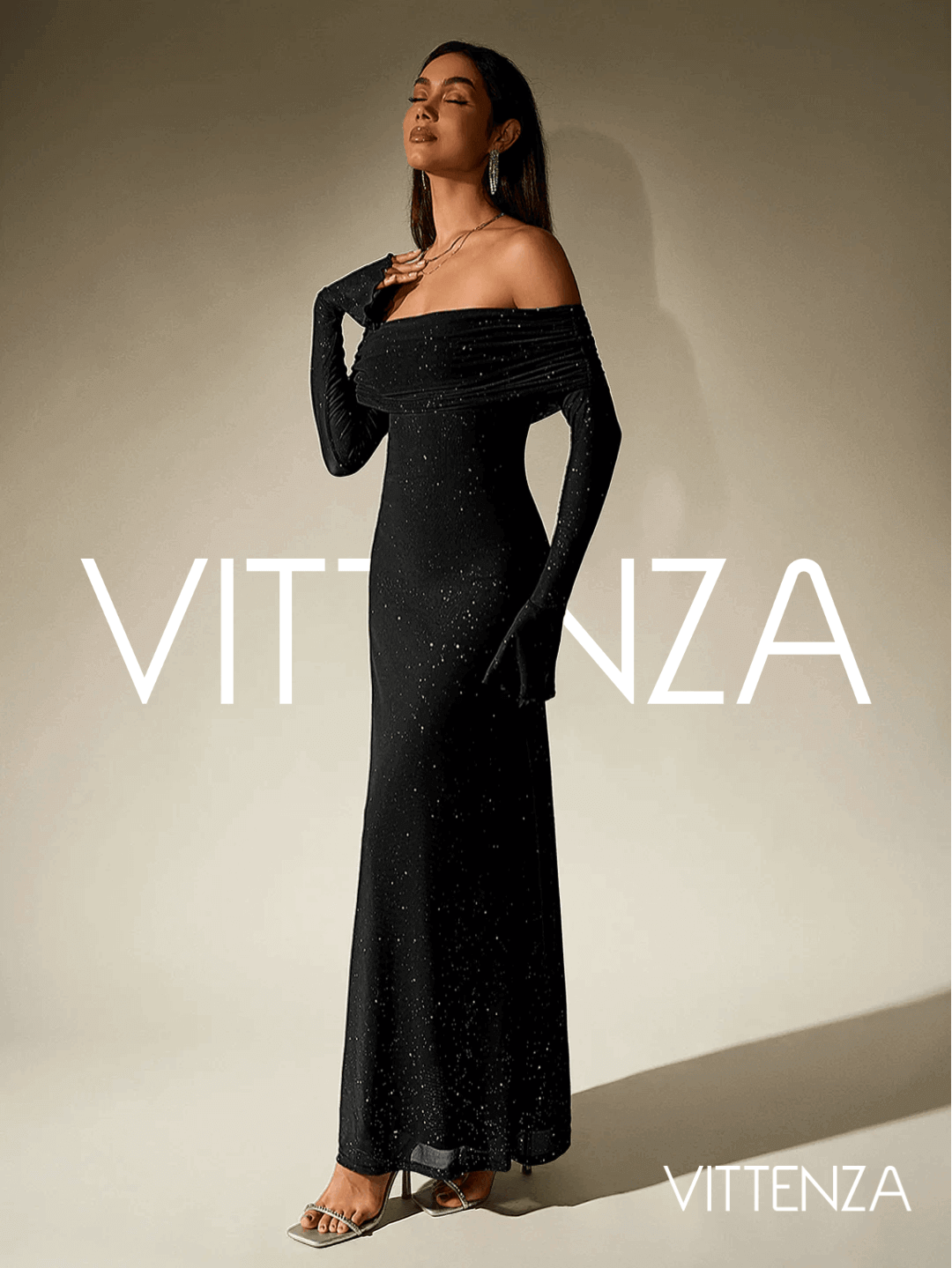 Side view of the Stellar Sparkle Maxi Dress in shimmering black, showcasing the off-shoulder design, long sleeves, and a floor-length silhouette. The model pairs the dress with metallic heels, statement earrings, and layered necklaces.