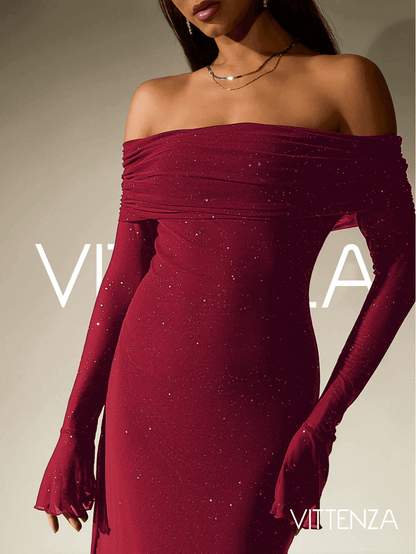 Close-up view of the Stellar Sparkle Maxi Dress in shimmering red, showcasing the off-shoulder design, glittering fabric, and flared cuffs on the long sleeves. The model pairs the look with delicate layered necklaces.